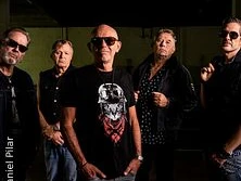 Fünf Männer posieren in dunkler Kleidung und Sonnenbrillen vor einem unscharfen Hintergrund.