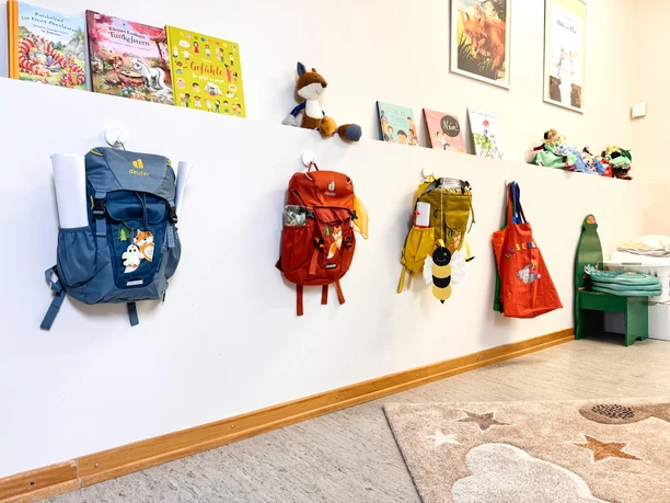 Bunte Kinderrucksäcke an der Garderobe unter einer Bilderbuchleiste im Kindergarten Amelinghausen.