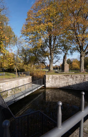 Nikolausquelle Historische Brunnenanlage umgeben von herbstlichen Bäumen und einem Metallgeländer im Freien.