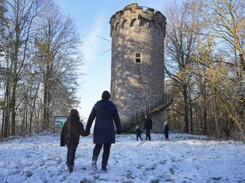 Immer auf der Hut 2 Verschneiter Rundturm im Wald mit Besuchergruppe im Vordergrund, kühler Wintertag voller Natur.