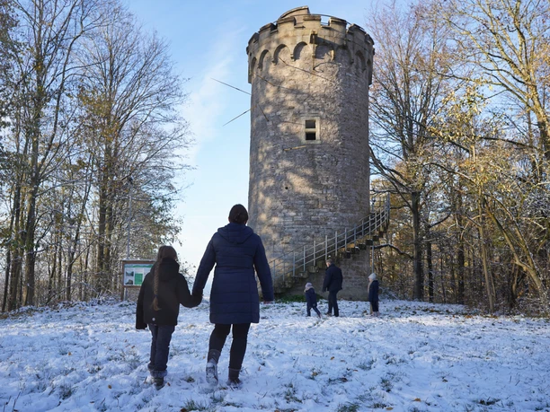 Immer auf der Hut 2 Verschneiter Rundturm im Wald mit Besuchergruppe im Vordergrund, kühler Wintertag voller Natur.