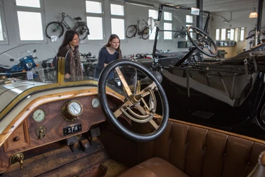 Automuseum Melle Im Automuseum Melle sind historische Autos in einem hellen Raum ausgestellt. Menschen betrachten die Fahrzeuge.