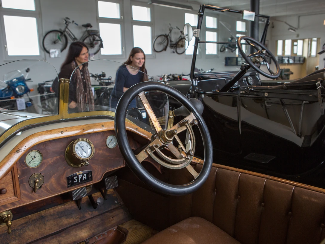 Automuseum Melle Im Automuseum Melle sind historische Autos in einem hellen Raum ausgestellt. Menschen betrachten die Fahrzeuge.