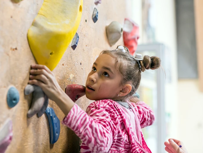 Junior Climber hanging on holds on climbing wall Junior Climber hanging on holds on climbing wall