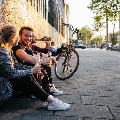 Tři mladí lidé sedí uvolněně s nápoji v rukou v restauraci Westwerk na Karl-Heine-Straße v módní lipské čtvrti Plagwitz.