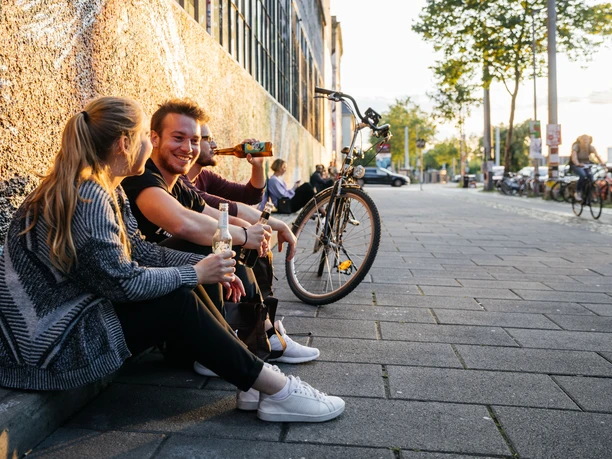 Tři mladí lidé sedí uvolněně s nápoji v rukou v restauraci Westwerk na Karl-Heine-Straße v módní lipské čtvrti Plagwitz.