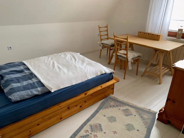 Ferienwohnung Hügel Schlafzimmer Ein helles Schlafzimmer mit Holzbett, passendem Tisch und Stühlen, dazu ein Teppich am Boden.