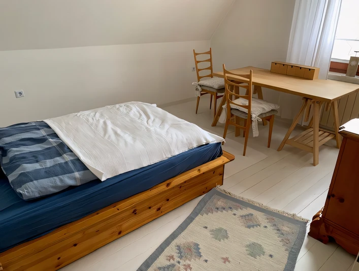 Ferienwohnung Hügel Schlafzimmer Ein helles Schlafzimmer mit Holzbett, passendem Tisch und Stühlen, dazu ein Teppich am Boden.