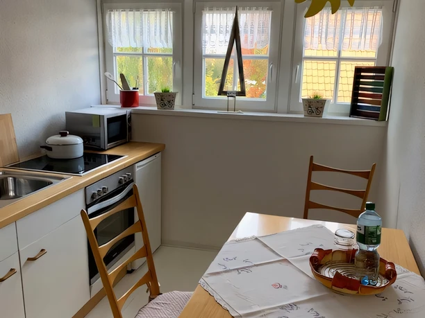 Ferienwohnung Hügel Küche Helle Küche mit Esstisch, zwei Stühlen, Herd, Mikrowelle, Schränken, und Fenstern mit Sichtschutz.