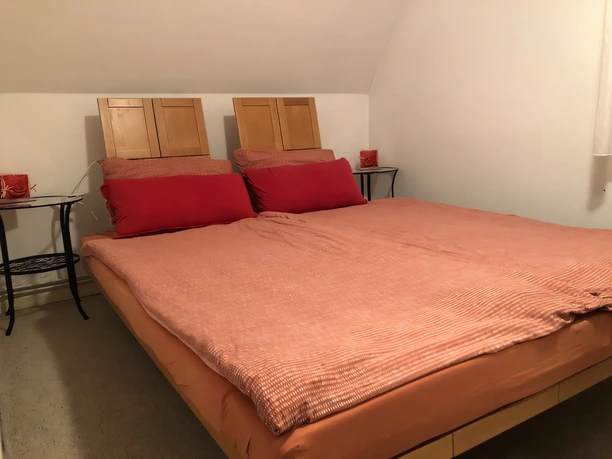 Schlafzimmer Kuhls Zwei Einzelbetten mit roten Kopfkissen und Tagesdecke, flankiert von schwarzen Nachttischen.