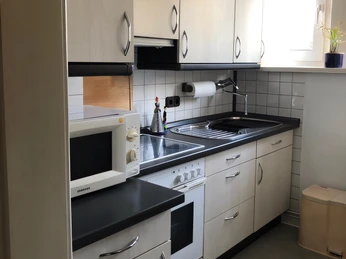 Küche Kuhls Helle, funktionale Einbauküche mit Herd, Mikrowelle, Spüle und weißen Fronten unter Tageslicht.