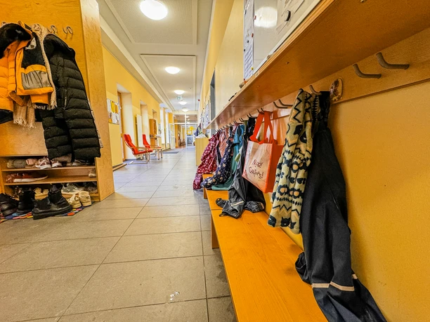 Kinderkrippe-Amelinghausen-01.jpg Hell erleuchteter Flur einer Kinderkrippe mit Holzgarderoben, Jacken und Sitzbänken.