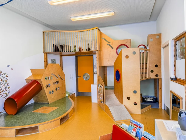Kinderkrippe-Amelinghausen-20.jpg Spielbereich mit Holzburg, Rutsche und Kletterpodesten in hellem Gruppenraum.