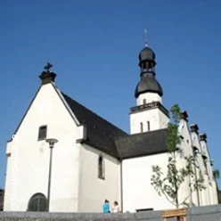 Die Aufnahme zeigt eine kleine, historische Kirche mit markantem Zwiebelturm unter strahlend blauem Himmel.