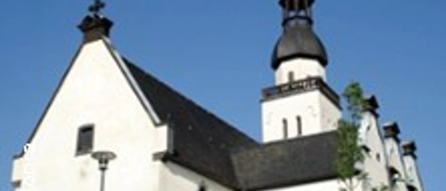 Die Aufnahme zeigt eine kleine, historische Kirche mit markantem Zwiebelturm unter strahlend blauem Himmel.