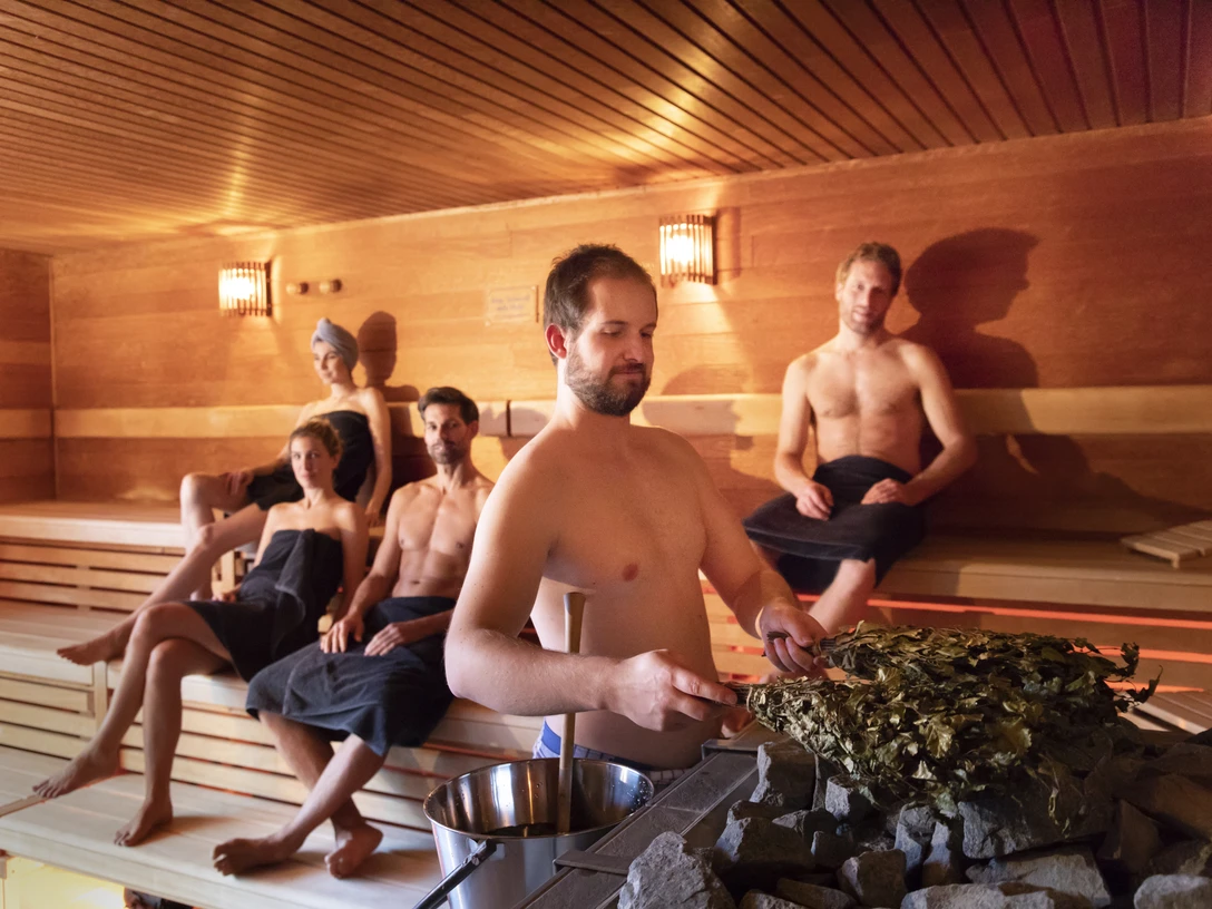 Koppke - Das neue Saunabad in Greetsiel Innenaufnahme von der Sauna im Koppke Greetsiel, vier Gäste entspannen, ein Saunameister bereitet den Aufguss vor