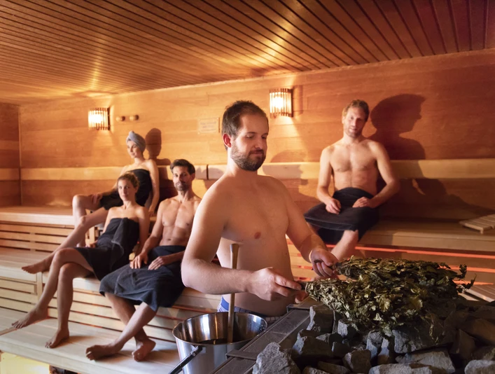 Koppke - Das neue Saunabad in Greetsiel Innenaufnahme von der Sauna im Koppke Greetsiel, vier Gäste entspannen, ein Saunameister bereitet den Aufguss vor