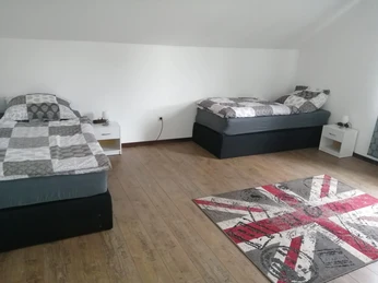 FWApartment_a_Teich_Schlafzimmer2_CC-BY-SA_Teutoburger_Wald_Stadt_Schloss_Holte-Stukenbrock.jpg.jpg Zwei Einzelbetten mit karierten Bettdecken in einem schlichten, hellen Zimmer mit Laminatboden.