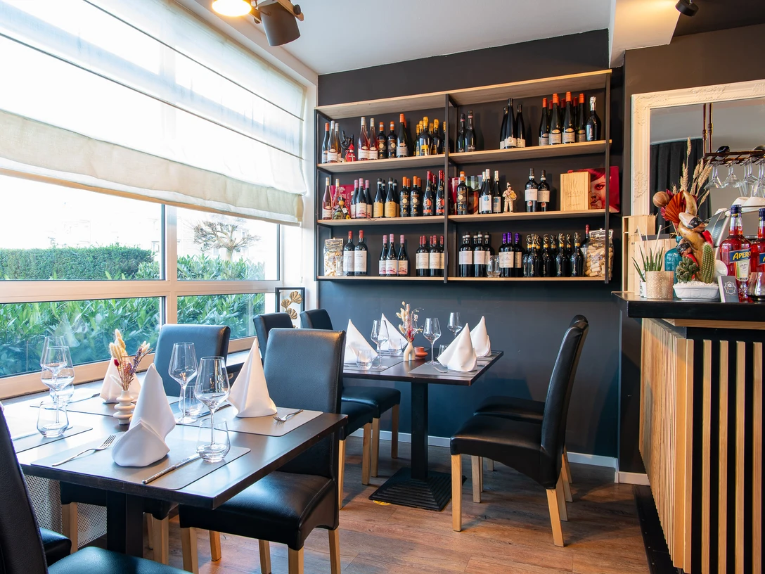 Tables covered with cloth napkins, a shelf on the wall with various bottles of wine