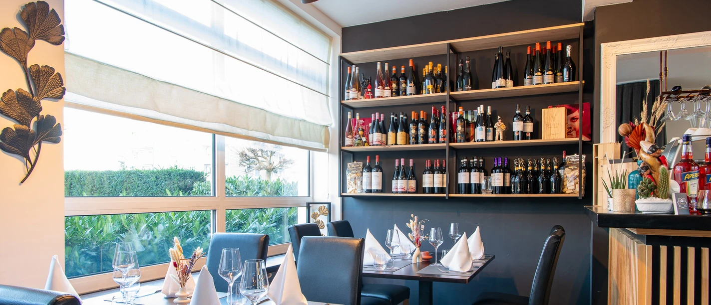 Tables covered with cloth napkins, a shelf on the wall with various bottles of wine