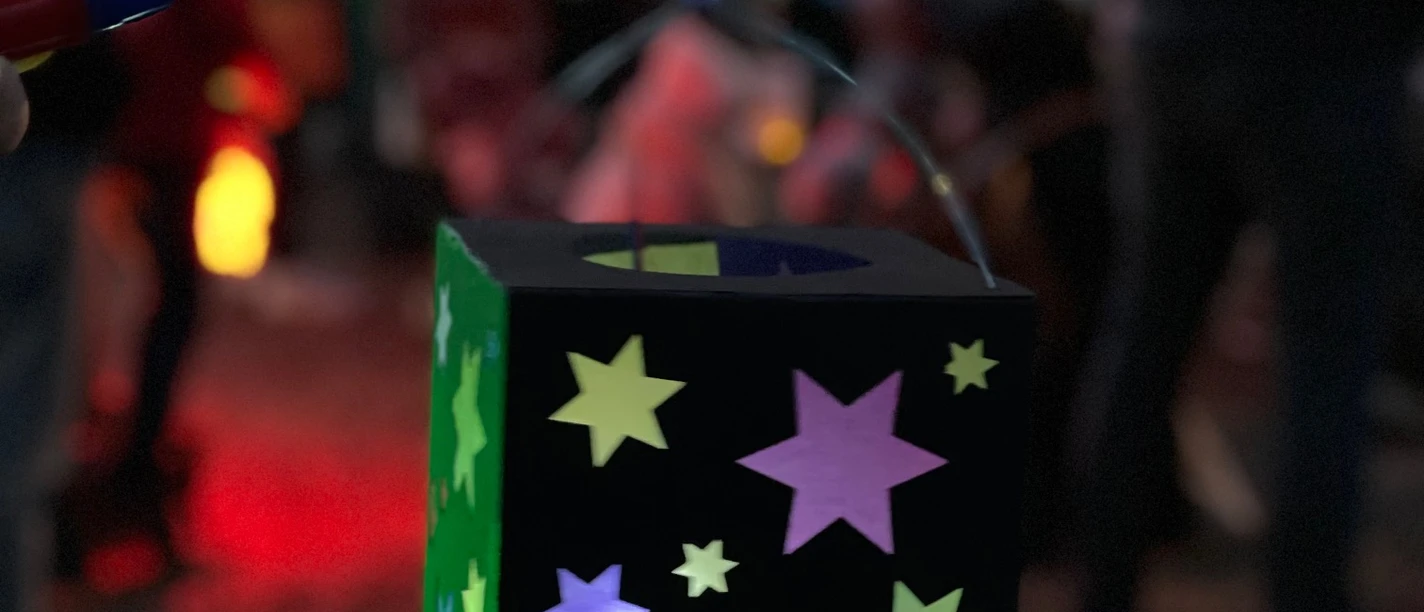 IMG_7403.jpg Eine bunte Laterne mit leuchtenden Sternen hängt an einem Stab während eines abendlichen Umzugs.