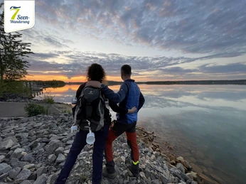 7-Seen-Wanderung©Sportfreunde_Neuseenland (3)_web.jpg Wanderer genießen bei Sonnenaufgang den Blick auf einen ruhigen See mit wolkenverhangenem Himmel.Hikers enjoy the view of a calm lake with a cloudy sky at sunrise.Turisté si užívají pohled na klidné jezero se zataženou oblohou při východu slunce.Wędrowcy cieszą się widokiem spokojnego jeziora z zachmurzonym niebem o wschodzie słońca.Wandelaars genieten van het uitzicht op een rustig meer met een bewolkte hemel bij zonsopgang.Gli escursionisti si godono la vista di un lago calmo con un cielo nuvoloso all'alba.