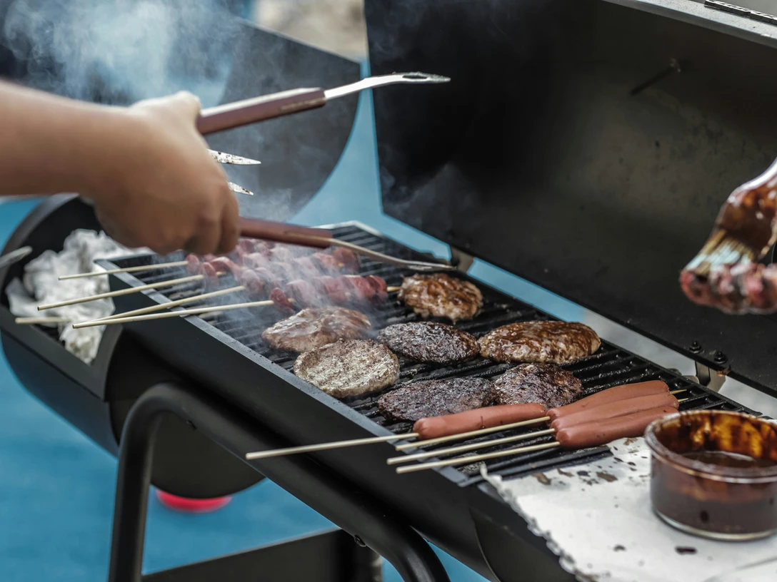 pexels-luis-quintero-1857732.jpg Menschen grillen Fleisch und Würstchen auf einem heißen Grill im Freien bei geselliger Atmosphäre.