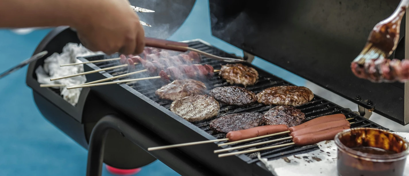 pexels-luis-quintero-1857732.jpg Menschen grillen Fleisch und Würstchen auf einem heißen Grill im Freien bei geselliger Atmosphäre.