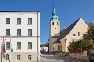 Stadtkirche St. Peter und Paul Sebnitz Weißes Rathausgebäude mit grünen Fensterrahmen und daneben eine Kirche mit grünem Turm vor blauem Himmel.