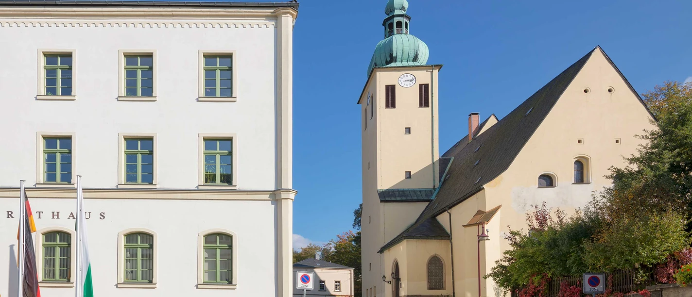 Stadtkirche St. Peter und Paul Sebnitz Weißes Rathausgebäude mit grünen Fensterrahmen und daneben eine Kirche mit grünem Turm vor blauem Himmel.