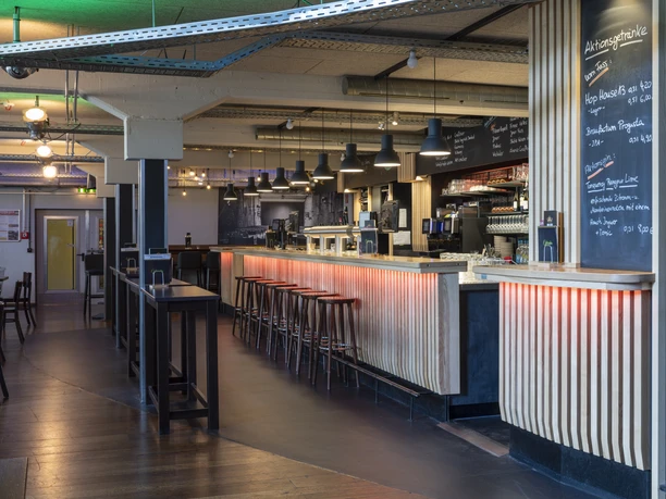 Gastronomiebereich Moderner Gastronomiebereich mit langer Theke, Barhockern und einladendem Ambiente.