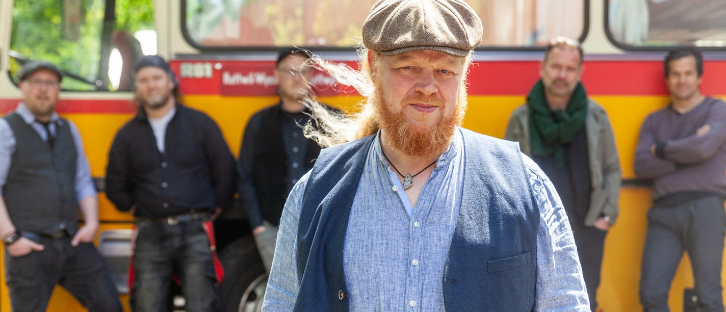 Wippsteert Sechs Männer stehen lässig vor einem gelben Bus; ein Mann im Vordergrund trägt eine Schiebermütze.