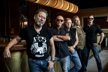 Die Band Extrabreit steht lässig in einer Bar, umgeben von eleganten Retro-Elementen und warmem Licht.