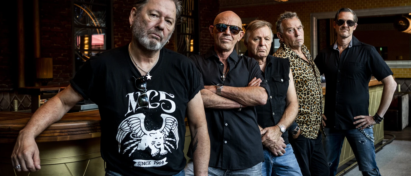 Extrabreit Die Band Extrabreit steht lässig in einer Bar, umgeben von eleganten Retro-Elementen und warmem Licht.