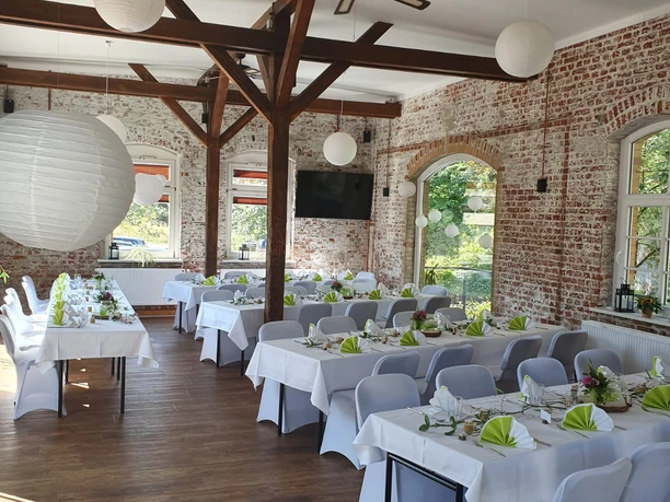 Saal Café Tender Heller Veranstaltungsraum mit Backsteinwänden, weiß gedeckten Tischen und grünen Servietten.