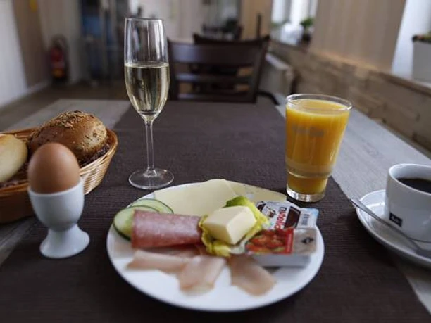 Eine Frühstücksplatte mit Aufschnitt, Käse und Butter, dazu ein Ei, Kaffee, Saft und ein Brötchenkorb.