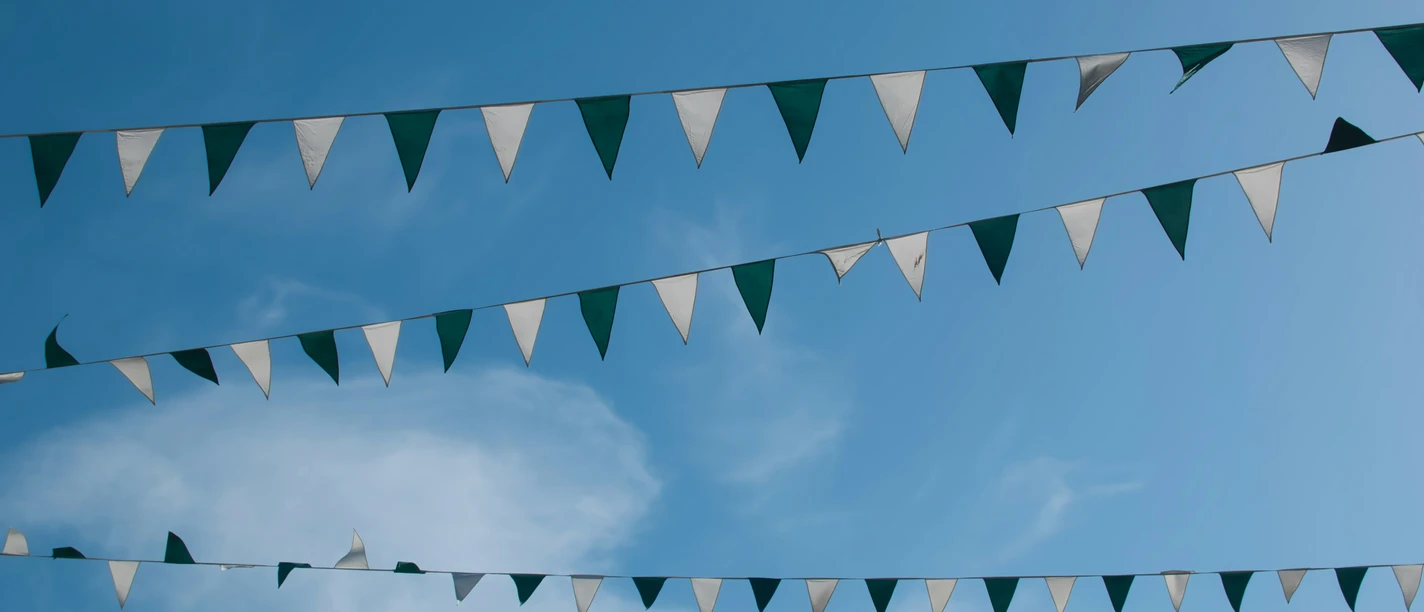 Girlanden unter blauem Himmel Grün-weiße Wimpelketten hängen im Wind vor blauem Himmel mit leichten weißen Wolken.