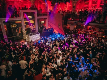 Alando Palais(c)next-choice 4.jpg Menschen tanzen in einem belebten, farbenfroh beleuchteten Nachtclub mit DJ auf einer erhöhten Bühne.People dance in a lively, colorfully lit nightclub with a DJ on a raised stage.Mensen dansen in een levendige, kleurrijk verlichte nachtclub met een DJ op een verhoogd podium.