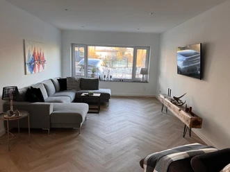 Moderner Wohnbereich mit Ecksofa, TV und großem Fenster, das viel Tageslicht hineinlässt.