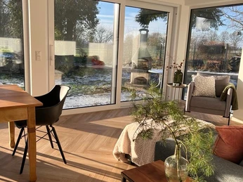 Moderne Wintergartenansicht mit großen Fenstern, Holzboden, stilvollen Möbeln und winterlichem Gartenblick.