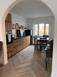 Moderne Küche mit Holzelementen, Esstisch für vier Personen und großem Fenster, das Tageslicht einlässt.