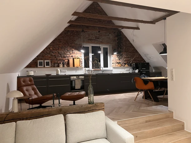 Moderne Loftküche mit Backsteinwand, Dachschrägen, Ledersessel, Esstisch und naturbelassenem Holzboden.