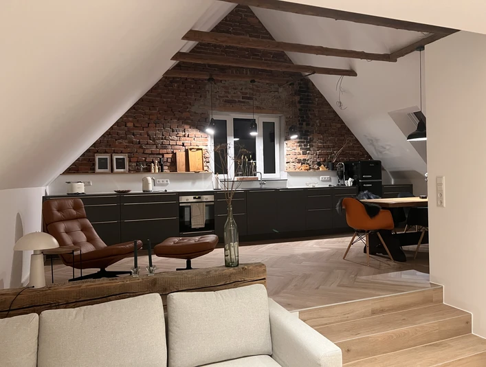Moderne Loftküche mit Backsteinwand, Dachschrägen, Ledersessel, Esstisch und naturbelassenem Holzboden.