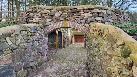 Ruine Windmühle Bruneforth, Stavern ©Naturpark Hümmling (8).jpg Steinbogen mit Rundbogenmauer aus Feldsteinen, umgeben von Bäumen im Naturpark Hümmling.