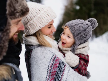 Familie im Winter © AdobeStock_Halfpoint Father and mother with small child in winter nature, standing in the snow.