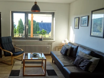 Ferienwohnung Jakobs Wohnzimmer Ein heller Wohnraum mit Sofa, Sessel, Couchtisch und großem Fenster mit Blick ins Grüne.