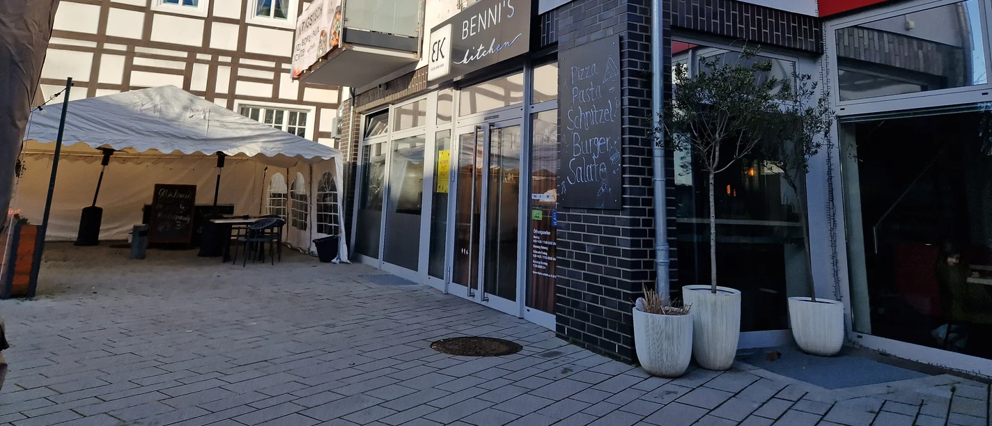 Restaurant Bennis Kitchen Delbrück Bennis Kitchen Delbrück: Modernes Restaurant mit Glasfassade, Sonnenschirmen und Fachwerkhaushintergrund.