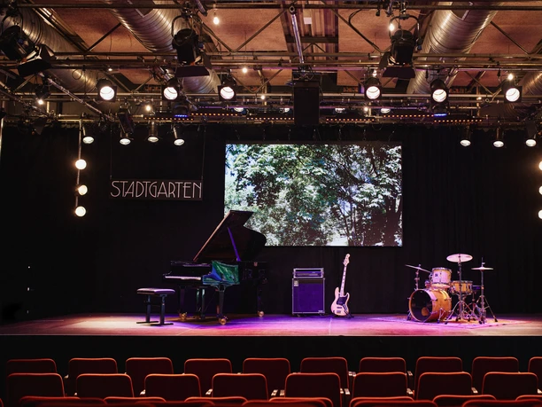 Stadtgarten A stage with a grand piano, guitar, drums and a "Stadtgarten" sign in the background.