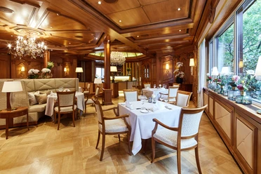 Elegantes Restaurant mit Holzvertäfelung, Kristallleuchtern und weiß gedeckten Tischen.
