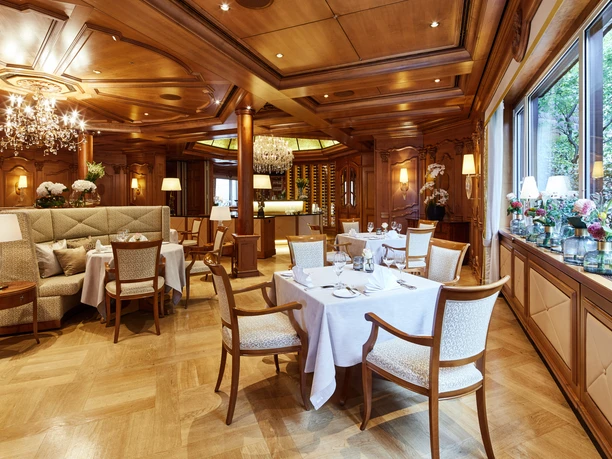Elegantes Restaurant mit Holzvertäfelung, Kristallleuchtern und weiß gedeckten Tischen.